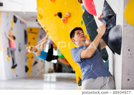 Male mountaineer climbing artificial rock wall without his belay indoors Male mountaineer climbing artificial rock wall without his belay indoors 88934977