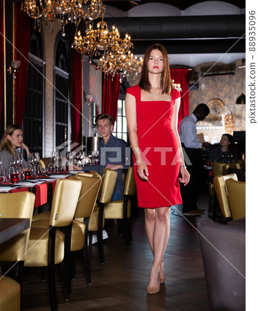 Attractive young woman in red dress walks through hall of a fashionable restaurant 88935096
