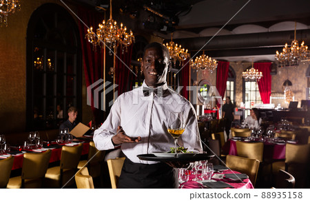 Portrait of African waiter in white shirt holding tray with dish and glass of white wine Portrait of African waiter in white shirt holding tray with dish and glass of white wine 88935158