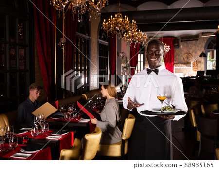 Portrait of African waiter in white shirt holding tray with dish and glass of white wine 88935165