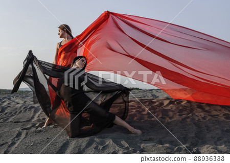 Two girls in black and red flowing fabric pose on sand dune Two girls in black and red flowing fabric pose on sand dune 88936388