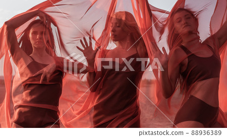 Three girls in red flowing fabric pose on sand dune 88936389