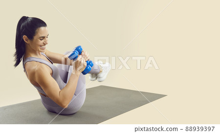 Athletic woman training with dumbbells on fitness mat isolated on light beige background. Athletic woman training with dumbbells on fitness mat isolated on light beige background. 88939397