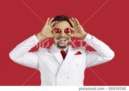 Handsome lucky man smiling and covering both his eyes with two red poker chips in hands, standing on red studio background, copyspace . Casino and gambling concept 88939398