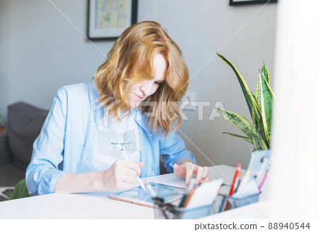 Young woman with red hair Illustrator web designer draws on tablet at desk at the home office Young woman with red hair Illustrator web designer draws on tablet at desk at the home office 88940544