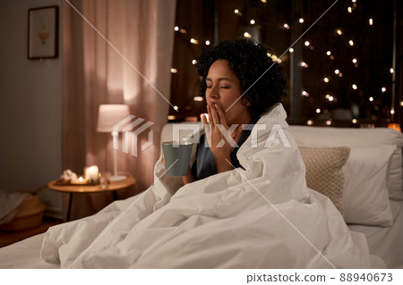 tired woman with coffee yawning in bed at night tired woman with coffee yawning in bed at night 88940673