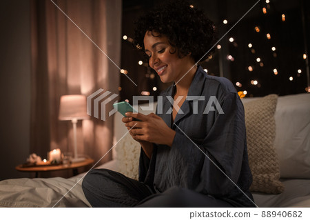 happy woman in pajamas with phone in bed at night happy woman in pajamas with phone in bed at night 88940682