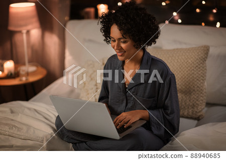 happy woman with laptop sitting in bed at night happy woman with laptop sitting in bed at night 88940685