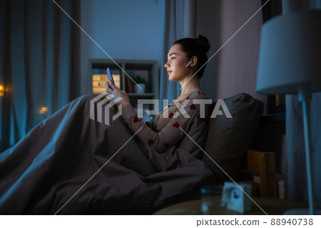 teenage girl with phone and earphones in bed teenage girl with phone and earphones in bed 88940738