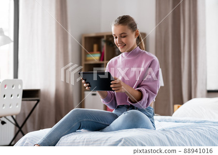 smiling girl with tablet pc sitting on bed at home 88941016