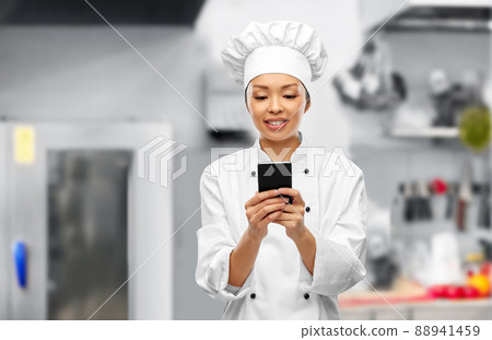 smiling female chef with smartphone in kitchen smiling female chef with smartphone in kitchen 88941459
