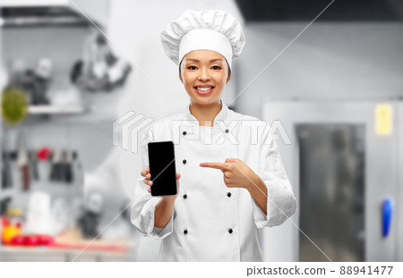 smiling female chef with smartphone in kitchen smiling female chef with smartphone in kitchen 88941477