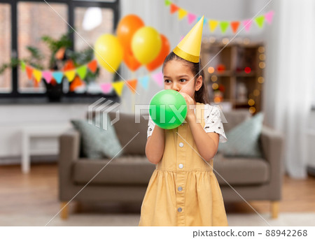 girl blowing balloon at birthday party at home 88942268