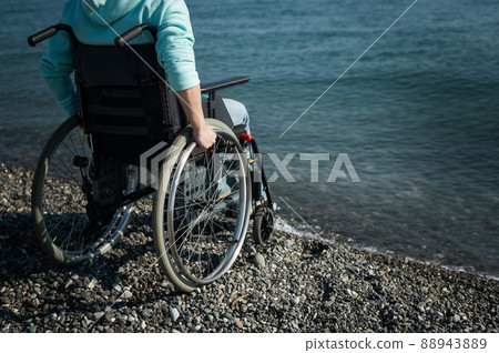 Caucasian woman in a wheelchair on the seashore. Close-up of female hands. 88943889