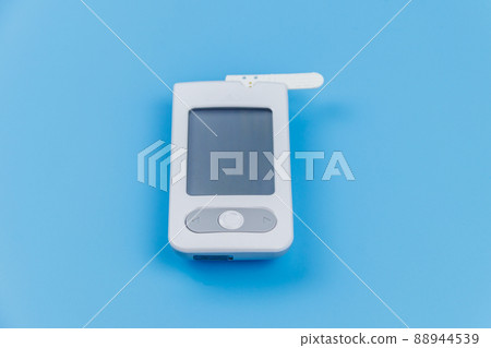 Digital glucometer with test strip on a pastel blue background. Diabetes concept 88944539