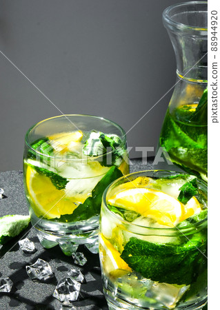 Mojito refreshing cocktail, alcohol drink. Lemonade with lemon and mint leaves on dark background. Trendy shadows Ice cubes. Summer refreshing detox drinks. Clean eating, healthy lifestyle concept. Mojito refreshing cocktail, alcohol drink. Lemonade with lemon and mint leaves on dark background. Trendy shadows Ice cubes. Summer refreshing detox drinks. Clean eating, healthy lifestyle concept. 88944920