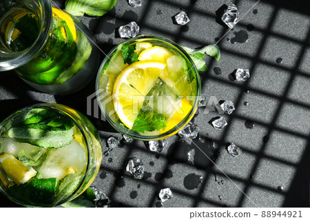 Mojito refreshing cocktail, alcohol drink. Lemonade with lemon and mint leaves on dark background. Trendy shadows Ice cubes. Summer refreshing detox drinks. Clean eating, healthy lifestyle concept. Mojito refreshing cocktail, alcohol drink. Lemonade with lemon and mint leaves on dark background. Trendy shadows Ice cubes. Summer refreshing detox drinks. Clean eating, healthy lifestyle concept. 88944921