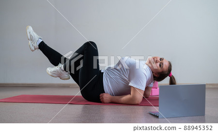 A chubby young woman is watching an online fitness lesson on a laptop. Distance sports training. A chubby young woman is watching an online fitness lesson on a laptop. Distance sports training. 88945352