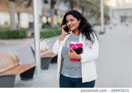 An Indian girl is walking around the city and talking on the phone. An Indian girl is walking around the city and talking on the phone. 88945633