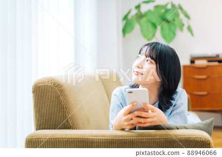 一個女人躺在沙發上，看著她的智能手機 88946066