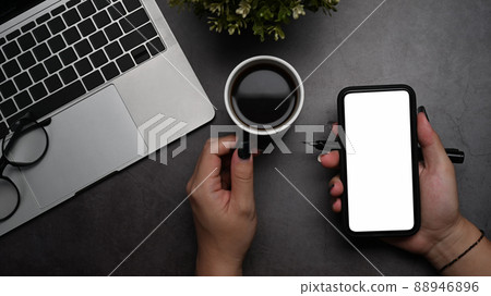 Above view woman hand holding mobile phone with empty screen on dark background. Above view woman hand holding mobile phone with empty screen on dark background. 88946896