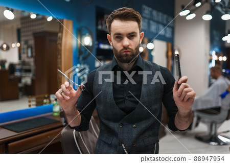 Brutal barber master with scissors and a comb in hands Brutal barber master with scissors and a comb in hands 88947954