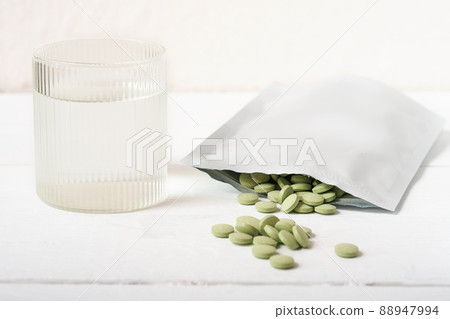 barley grass pills on a table next to glass of water. Spirulina and chlorella tablets for detox and metabolism supplement. raw vegan superfood. barley grass pills on a table next to glass of water. Spirulina and chlorella tablets for detox and metabolism supplement. raw vegan superfood. 88947994