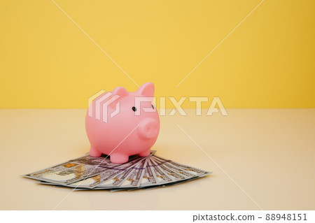 Pink piggy bank with dollar banknotes on yellow background. Savings concept Pink piggy bank with dollar banknotes on yellow background. Savings concept 88948151