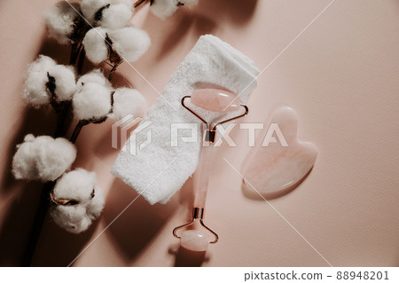 Skin care concept. Jade face roller for beauty facial massage therapy with towel and cotton on a pink background. Skin care concept. Jade face roller for beauty facial massage therapy with towel and cotton on a pink background. 88948201