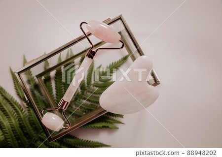 Massage roller and Gua sha massage scraper with a tropical leaf. Beauty image. Top view Massage roller and Gua sha massage scraper with a tropical leaf. Beauty image. Top view 88948202