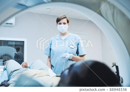 Female radiologist in mask and gloves pushing button on control panel while providing diagnostic imaging of patient 88948336