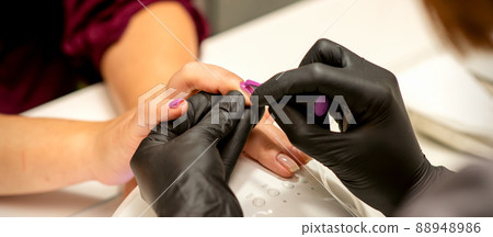 Professional manicure. A manicurist is painting the female nails of a client with purple nail polish in a beauty salon, close up. Beauty industry concept Professional manicure. A manicurist is painting the female nails of a client with purple nail polish in a beauty salon, close up. Beauty industry concept 88948986