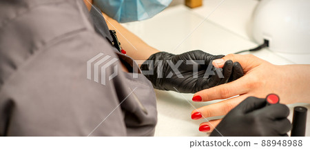 Professional manicure. A manicurist is painting the female nails of a client with red nail polish in a beauty salon, close up. Beauty industry concept Professional manicure. A manicurist is painting the female nails of a client with red nail polish in a beauty salon, close up. Beauty industry concept 88948988