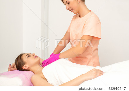 Beautician with a patient during sugaring. The cosmetologist waxes the female armpit 88949247