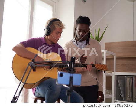 A personal afroamerican tutor explains to his asian student how to play studied chord correctly. Musical education at home A personal afroamerican tutor explains to his asian student how to play studied chord correctly. Musical education at home 88950276