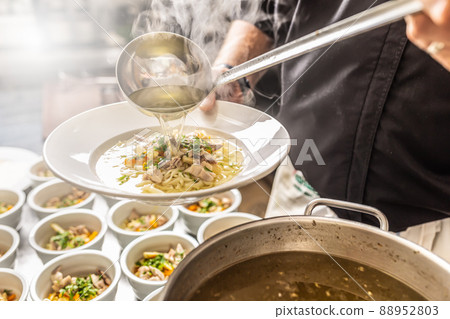 Chef pours broth into a chicken soup with noodles, meat and vegetable 88952803