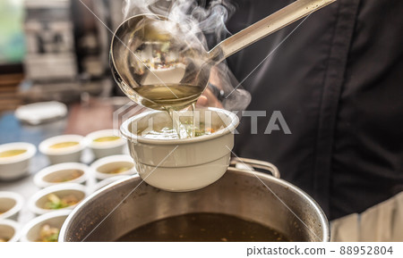 Chef pours broth into a chicken soup with noodles, meat and vegetable 88952804
