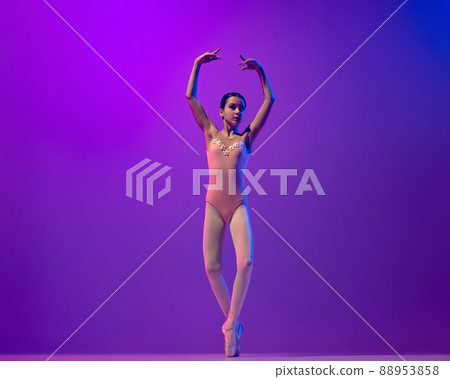 Portrait of young little ballet dancer, teen practicing, dancing isolated on purple background in neon light. Art, grace, beauty, ballet school concept Portrait of young little ballet dancer, teen practicing, dancing isolated on purple background in neon light. Art, grace, beauty, ballet school concept 88953858