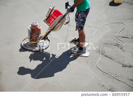 Close up of man builder using troweling machine while screeding floor. Worker finishing concrete surface with floor screed grinder machine at construction site on the roof of residential building. Close up of man builder using troweling machine while screeding floor. Worker finishing concrete surface with floor screed grinder machine at construction site on the roof of residential building. 88955957