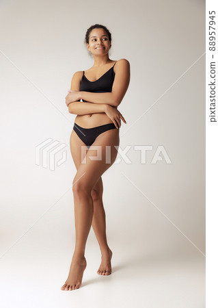 Full-length portrait of young slim woman posing in black underwear isolated over grey background Full-length portrait of young slim woman posing in black underwear isolated over grey background 88957945
