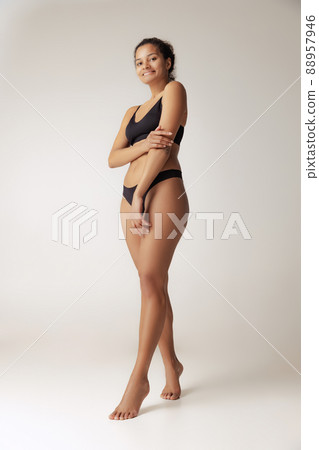 Full-length portrait of young slim woman posing in black underwear isolated over grey background. Depilation, epilation concept Full-length portrait of young slim woman posing in black underwear isolated over grey background. Depilation, epilation concept 88957946