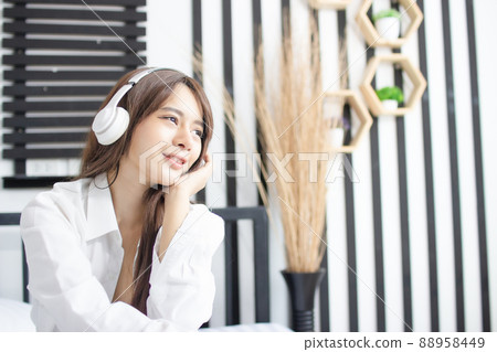 Portrait young smile happy beautiful asian woman relax bedroom. woman with headphones playing acoustic guitar in white bedroom 88958449