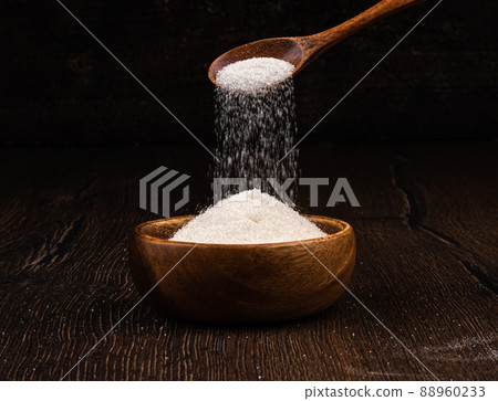 White granulated sugar is poured from a wooden spoon into a wooden bowl. 88960233