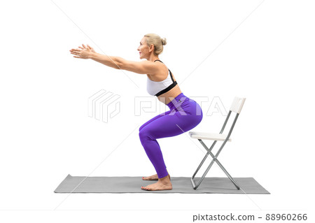 Exercises with props. Athletic caucasian woman in purple leggings practice squats using a chair, isolated on white. Exercises with props. Athletic caucasian woman in purple leggings practice squats using a chair, isolated on white. 88960266