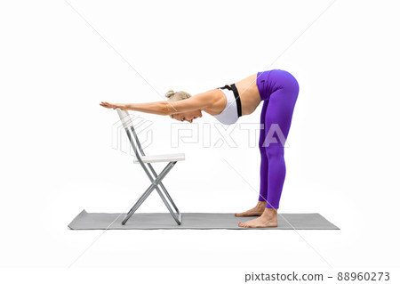 Iyengar yoga. Fit caucasian woman in purple leggings practice warrior pose  using a chair, isolated on white. Stock Photo