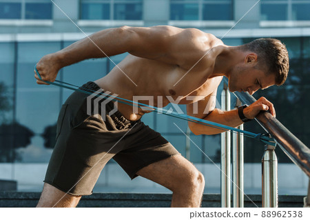 Muscular man during workout with a resistance rubber band on a street. Muscular man during workout with a resistance rubber band on a street. 88962538