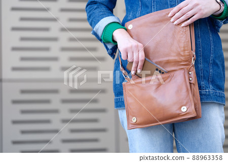 Woman putting mobile phone in brown leather handbag closeup 88963358