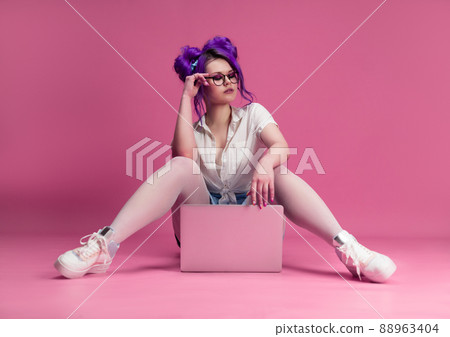 sexy girl with glasses and purple hair with a laptop on a pink background 88963404