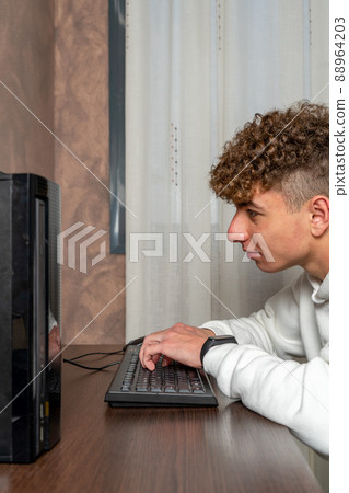 Vertical shot of a young man with curly hair typing concentrated on his desktop computer. 88964203