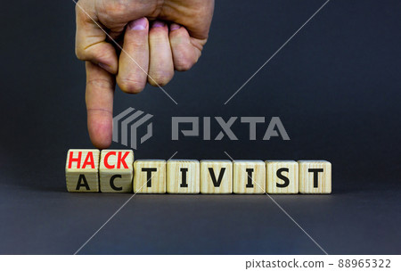 Activist or hacktivist symbol. Businessman turns wooden cubes and changes the word Activist to Hacktivist. Beautiful grey table grey background, copy space. Business activist or hacktivist concept. 88965322